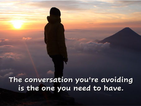 Person silhouetted on mountain peak at sunrise representing courage to face hard conversations