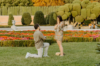 Woman reacting emotionally as partner kneels to propose in Parterre Gardens Retiro Park Madrid during surprise engagement.