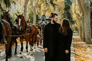 Engaged couple portrait on tree-lined path at Campo del Moro with horse carriage behind.