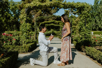 Man kneeling to propose in Retiro Park Madrid while girlfriend reacts surprised during romantic engagement photoshoot.