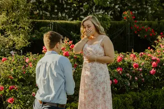 Woman covering her mouth in surprise during a marriage proposal at La Rosaleda rose garden in Retiro Park, Madrid.
