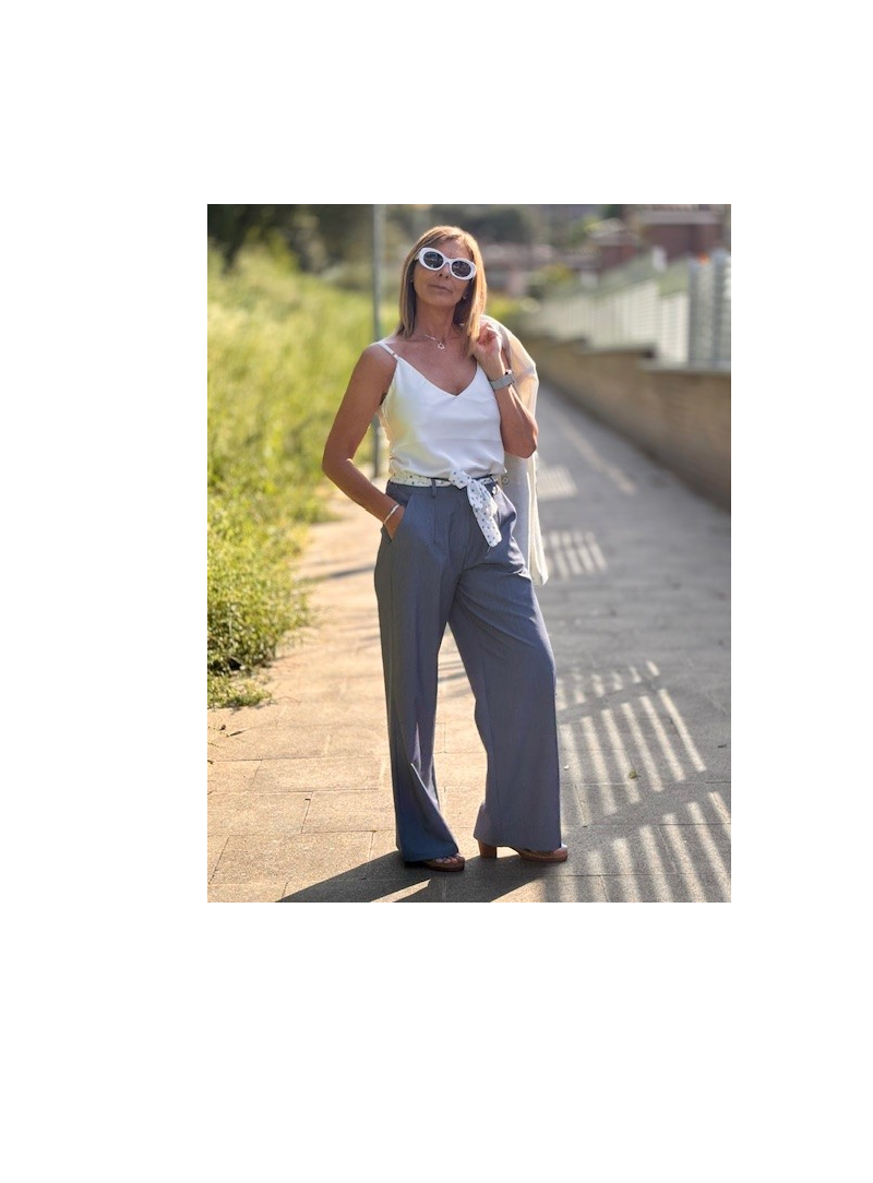 Mujer elegante con pantalones azules, blusa blanca y gafas de sol.