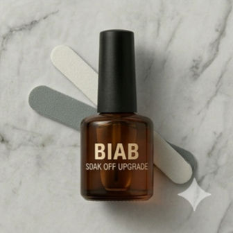 A professional square-ratio photograph of a minimalist white BIAB (Builder in a Bottle) bottle on a bright white marble background. The bottle features clean, black typography that reads "BIAB SOAK OFF UPGRADE." Behind the bottle, two aesthetic nail files—one grey and one white—are arranged at an angle, emphasizing the system's focus on natural nail health and professional growth journeys.