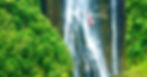 Red helicopter flies before a massive waterfall in lush rainforest on Hawaii’s Big Island.