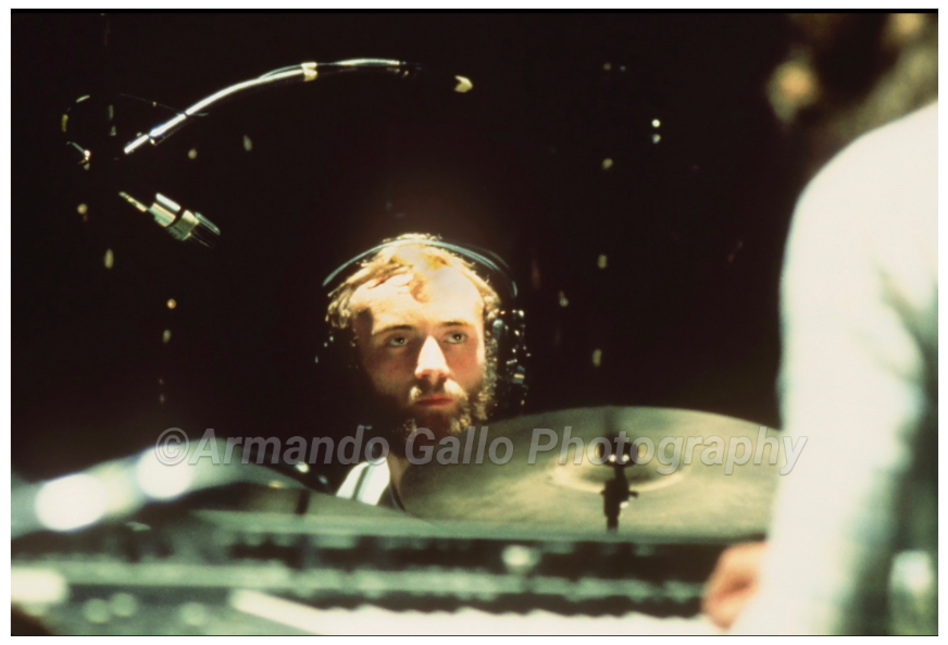 Phil Collins head showing above his drum cymbals in the foreground during live show