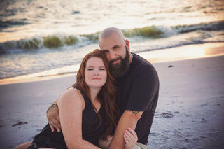bald man with beard embracing woman while sitting on the sand