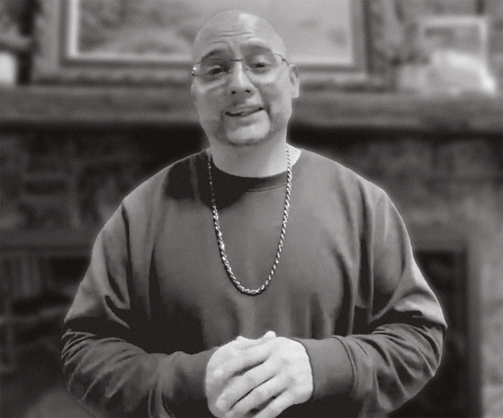 Man smiling, hands held together, looking at camera.