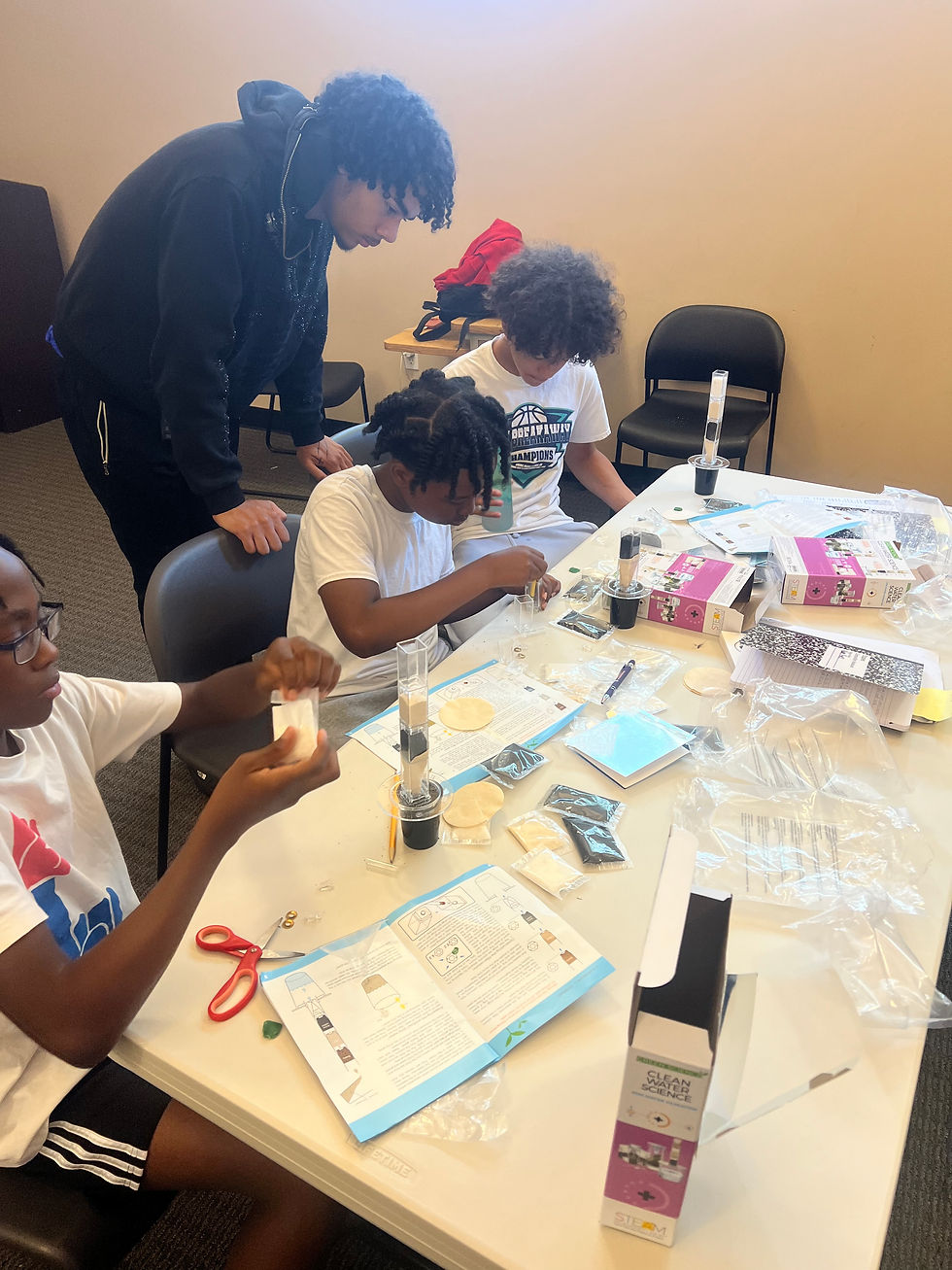 Kids and an adult assemble Clean Water Science STEM kits at a table, reading instructions and using tools in a classroom.