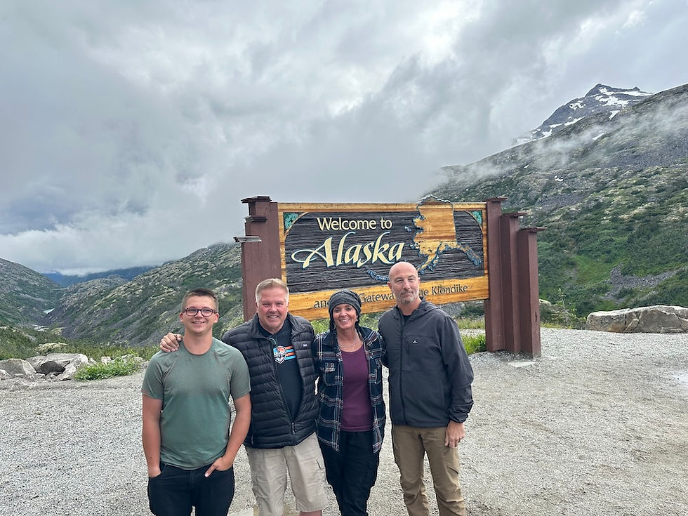 Tourists posing in front of the Welcome to Alaska sign