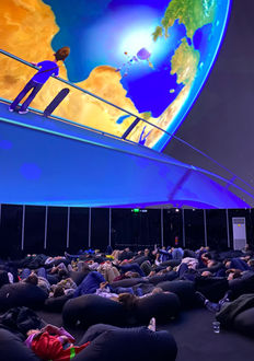 Público en butacas bajo una proyección fulldome del planeta Tierra