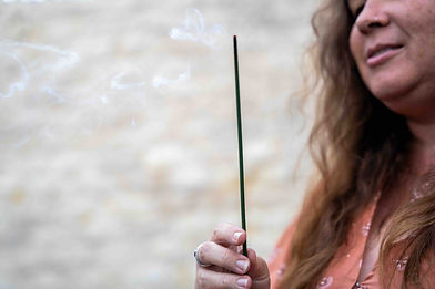 Lauren Dionysius holding a burning incense stick, with smoke rising gently beside her.