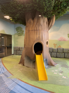A large tree sculpture in a childrens play area with yellow slide coming out of it.