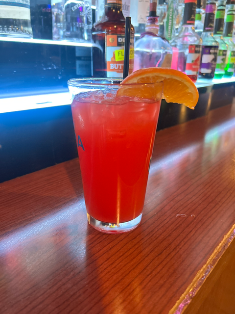Red cocktail with an orange slice on a bar