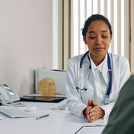 Woman in White Suit with Stethoscope Talking to a Person for General Medical Consultations.