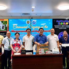 Eight people in a room smiling, holding signed documents for a Memorandum of Agreement. Background screens display colorful text and logos.