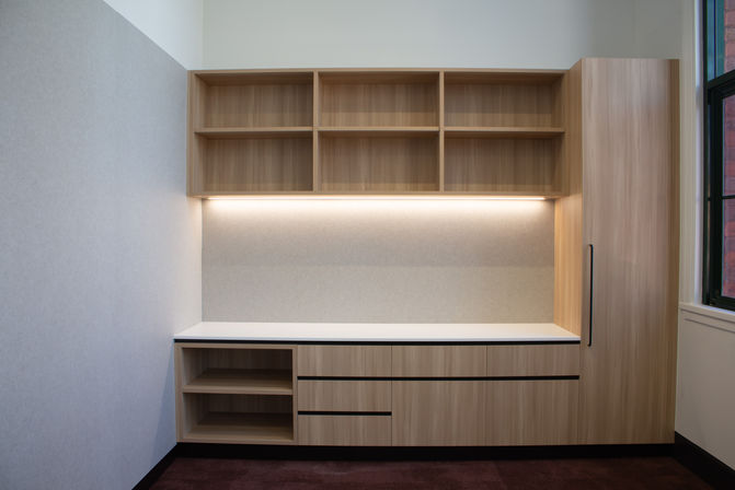 Timber cabinetry installed against full-height light grey acoustic wall panels.