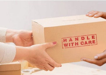 Closeup of hands of one woman handing another woman a package marked HANDLE WITH CARE