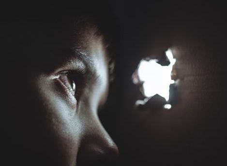 closeup of face of someone in darkness looking through a hole where light is showing through