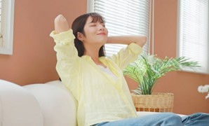 woman in a yellow blouse with eyes closed and a peaceful smile on her face, relaxing on a couch.