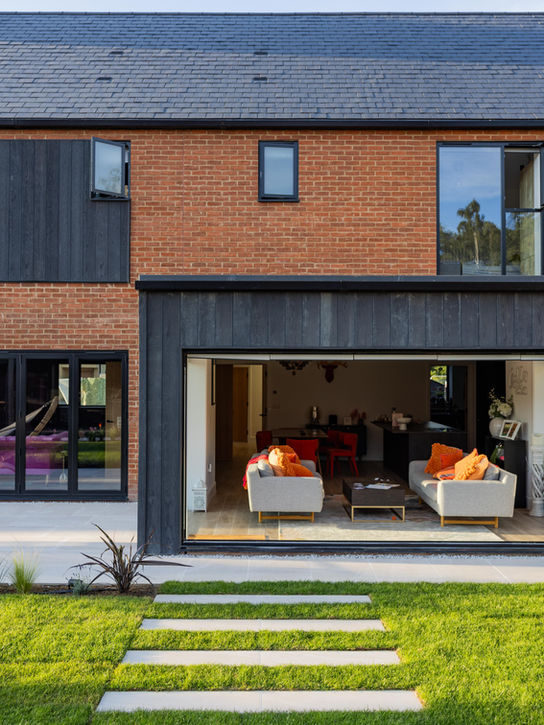 A luxury house with the patio and turf area of the back garden with plants along the edge