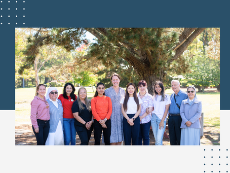 Group of people standing in front of a tree in a lush green garden on a sunny day