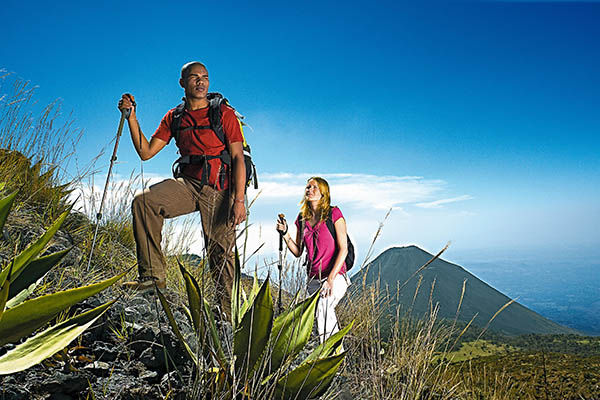 Deux randonneurs gravissant les pentes d’un volcan au Salvador, sous un ciel bleu dégagé.