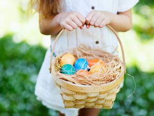 Child holding a woven Easter basket filled with colorful dyed eggs outdoors in spring, representing traditional Easter basket goodies.