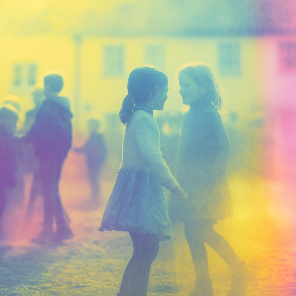 Deux fillettes discutent joyeusement, entourées d'autres enfants flous