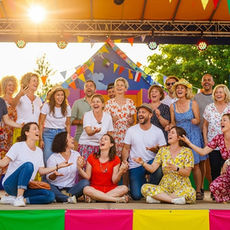 Un groupe joyeux de personnes de tous âges sur une scène colorée, en train de rire et de s’exprimer avec le corps.