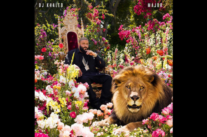 DJ Khaled sitting in a King throne chair with beautiful flowers and fierce lion by his side looking on.