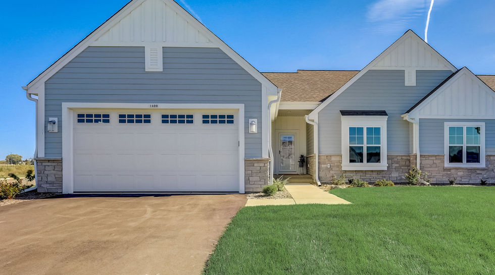 Asphalt drive leads up to white steel garage door of a duplex condo unit, green lawn, modern farmhouse style, large windows, asphalt shingle roof, white trim, light blue fiber cement siding