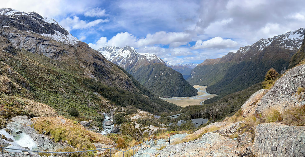 A rocky mountainside looks over a river winding between additional mountains in the distance.