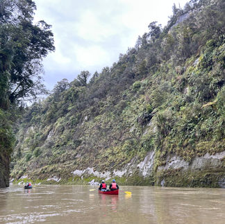 Two people canoeing down a river with steep, green walls on either side.