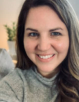 Smiling woman looking at the camera with long brown hair, grey sweater.