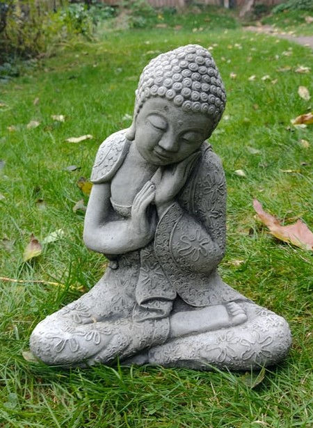 Small resting Buddha statue peacefully meditating on the green grass outdoors