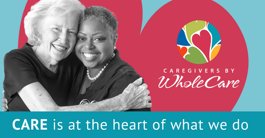 A senior white woman being hugged by a younger african american woman. There is a large red heart behind them on an aqua background. Text: CARE is at the heart of what we do. Caregivers by WholeCare