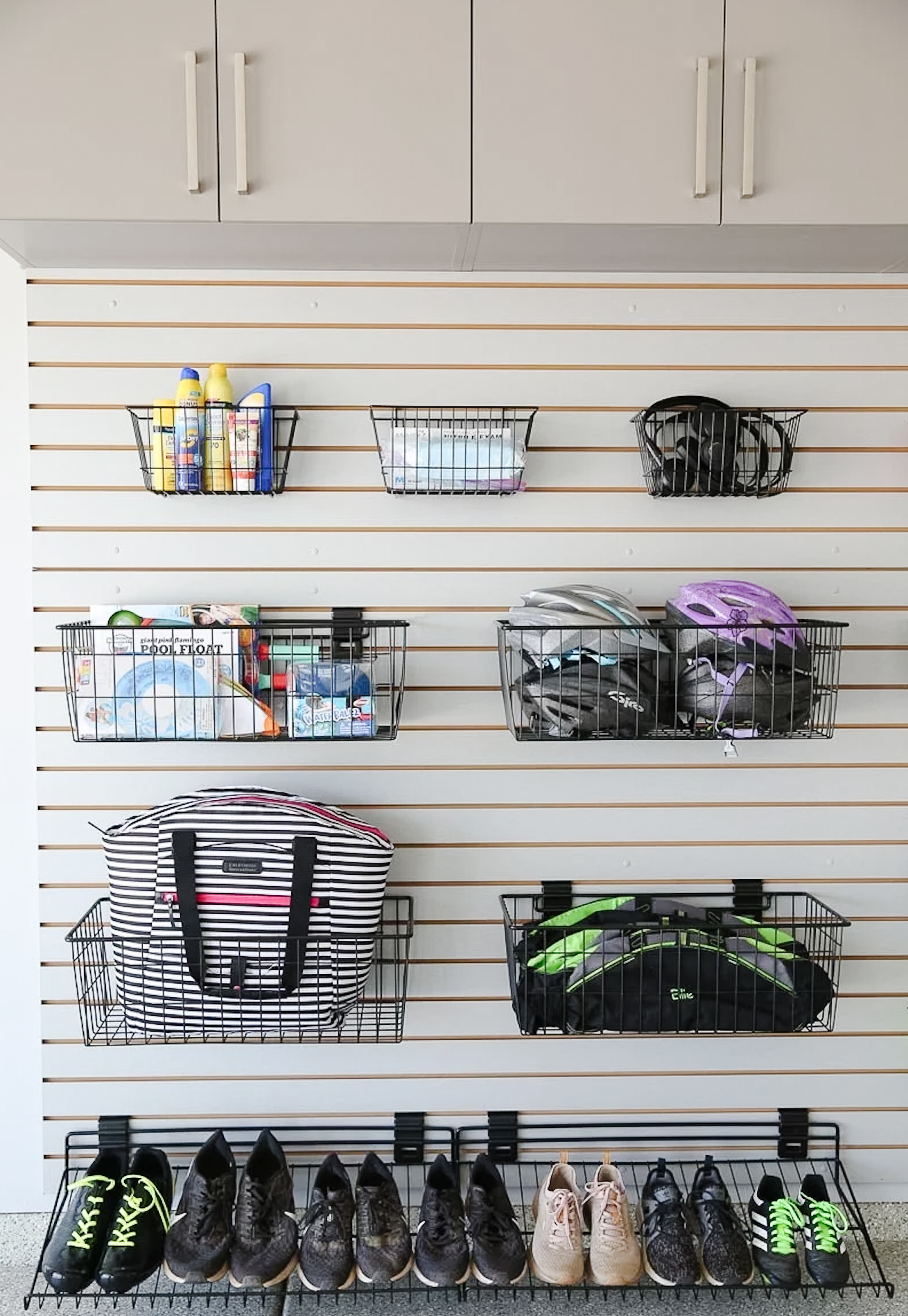 White slatwall with black wire baskets holding bike helmets, a striped tote bag, spray bottles and sports gear