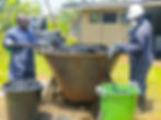 Two workers in safety gear shoveling charcoal into a kiln.