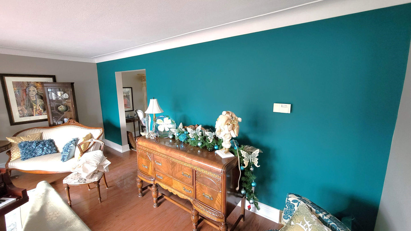 Teal wall with wooden cabinet, decor, and lamp in living room.