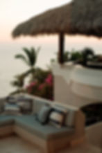 Mobiliario resistente a la humedad de clima costero. Se observa el mar y una palapa en la terraza de una residencia de lujo.