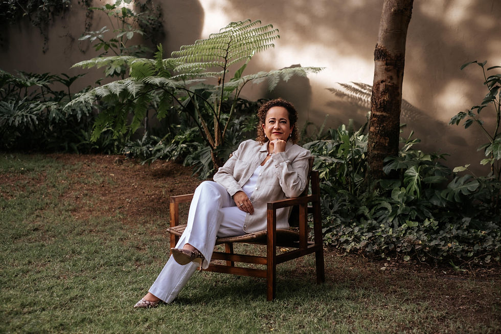 Diseñadora de interiores Victoria Plasencia sentada en una silla de madera, rodeada de vegetación.