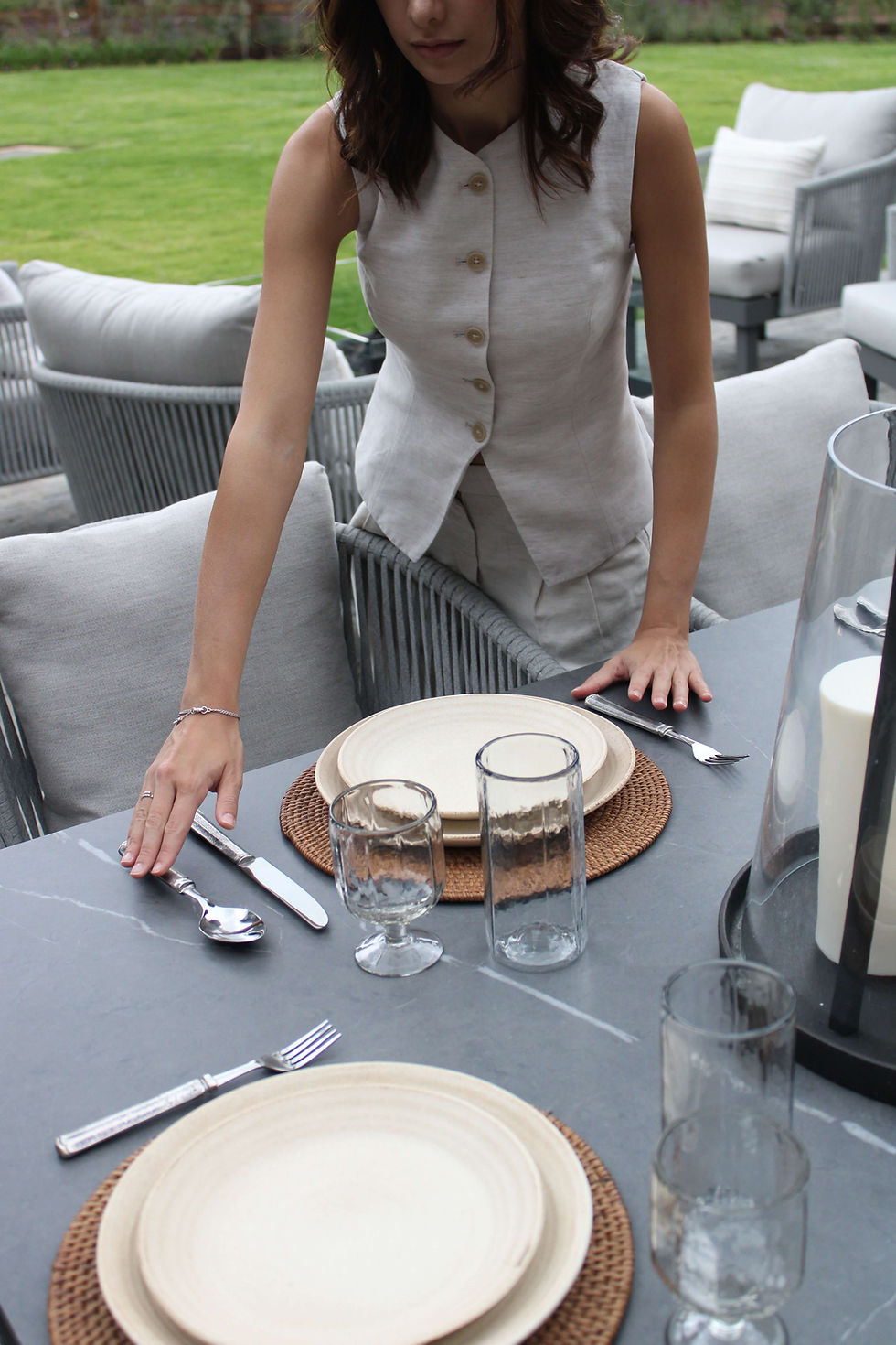Mujer montando una mesa de comedor al aire libre con vajilla neutra y decoración elegante.