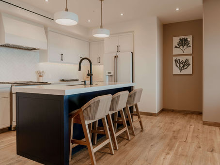 Cocina de lujo silencioso con isla central oscura, sillas de madera tejida y gabinetes blancos en diseño interior contemporáneo.