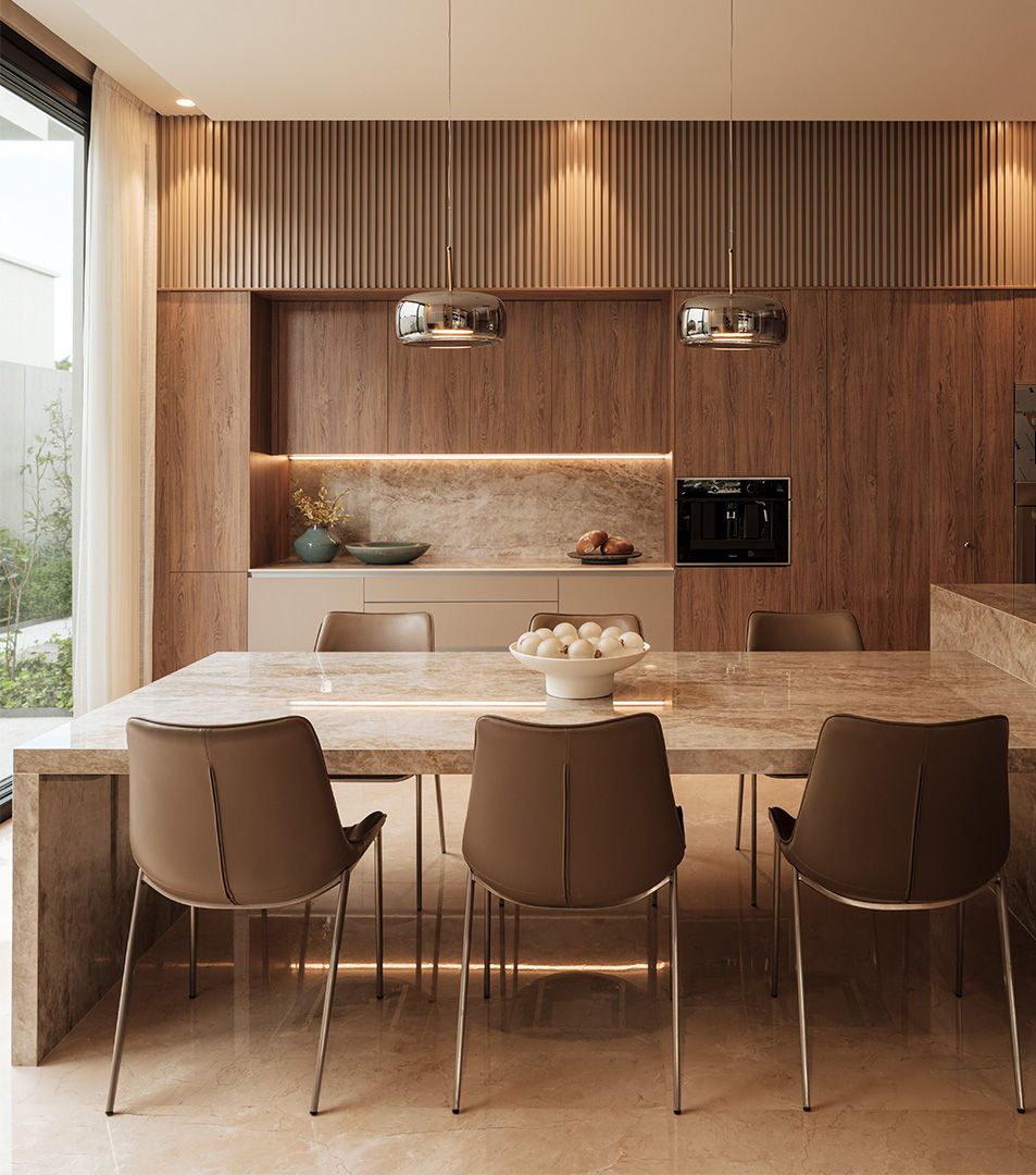 Dining area integrated with the kitchen, featuring a marble table, leather chairs, and linear pendant lights that balance warm materials.