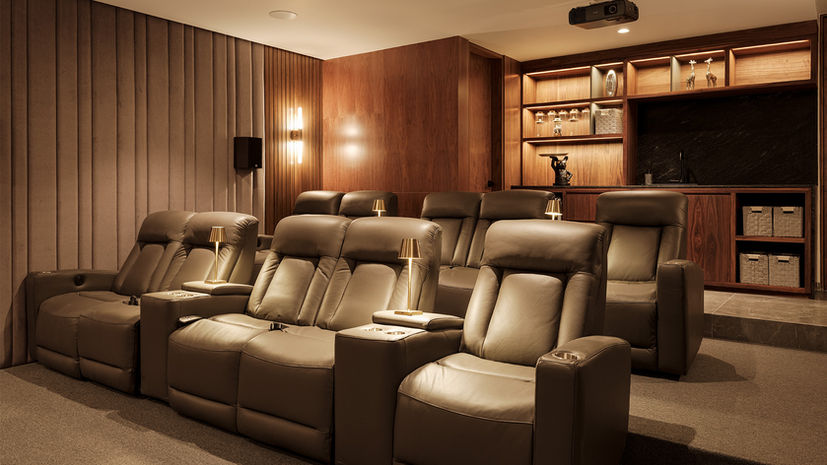 Sala de cine residencial con butacas reclinables de piel, revestimientos acústicos y carpintería en madera diseñada por un diseñador de interiores.