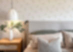 A beautifully staged bedroom scene with a minimalist wallpaper design featuring a white background and scattered pale green leaves
