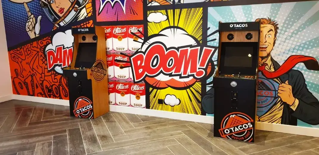 Bornes d'arcades devant un grand mur coloré façon bande dessinées. Dans un magasin Otacos