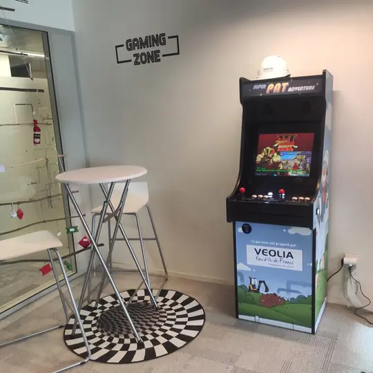 Console arcade personnalisée pour entreprise, intégrée dans un espace lounge, avec joysticks doubles et jeux classiques revisités