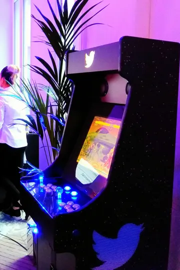 Borne multijeux premium avec branding corporate, deux joueurs, dans une salle de détente d’entreprise au design contemporain
