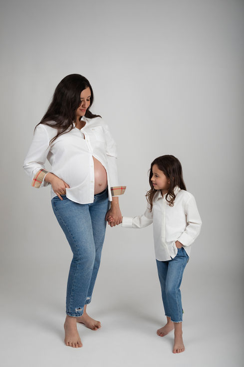 Future maman avec sa jeune fille se tenant la main et regardant vers son ventre.